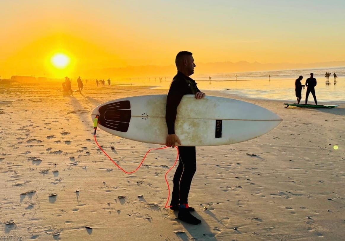 David with his surfboard on the beach at sunset